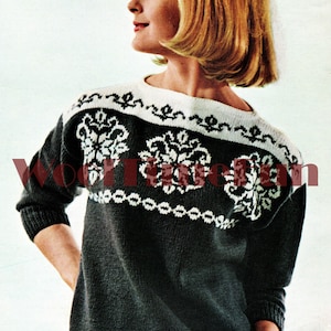 May include: A black and white knitted sweater with a floral pattern on the chest and a white trim around the neck. The sweater is being worn by a woman with short blonde hair.
