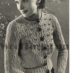 May include: A close-up of a woman wearing a gray knitted cardigan with a button-up front. The cardigan has a cable knit pattern and is styled with a simple, classic design.