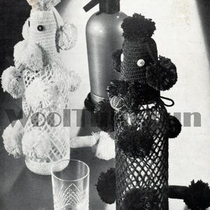 Puede incluir: Dos fundas de botella de caniche de ganchillo, una blanca y otra negra, con detalles de pompón. Un vaso transparente y un sifón de soda también están en la imagen. El caniche blanco tiene un diseño de encaje alrededor de la botella.