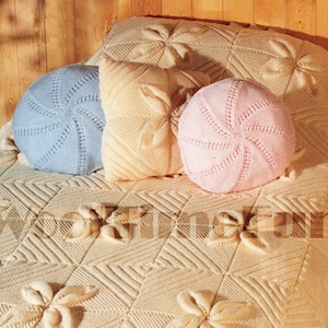 Può includere: Una coperta di maglia bianca con un motivo floreale e tre cuscini di maglia, uno blu, uno rosa e uno crema.