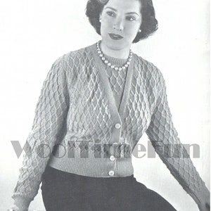 May include: A woman wearing a knitted cardigan with a diamond pattern. The cardigan has a V-neck and buttons down the front. She is wearing a pearl necklace.