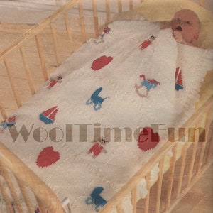 Könnte beinhalten: Eine weiße gestrickte Babydecke mit verschiedenen bunten gestickten Designs, darunter ein Segelboot, ein Schaukelpferd, ein Herz und ein Kinderwagen. Die Decke liegt in einem Holzbettchen mit einem Baby darauf.
