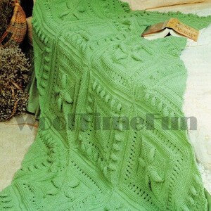 May include: A green crocheted throw blanket with a textured pattern and fringe edging. The blanket is draped over a bed with a book on top.