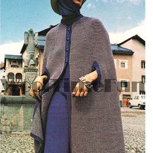 May include: A woman wearing a long, knitted cape with a white hat and a blue dress. The cape has a geometric pattern and is a light brown and white color. The dress is a dark blue color and has a long, flowing skirt.