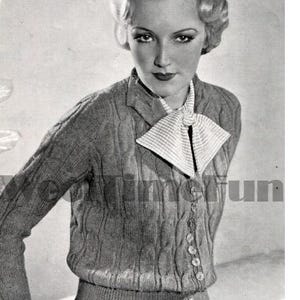 May include: A black and white photo of a woman wearing a knitted cardigan with a cable knit pattern and a white bow tie. The cardigan has a button closure and a ribbed hem.