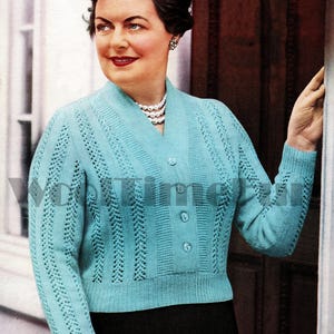 May include: A light blue knitted cardigan with a V-neck and button closure. The cardigan has a delicate lace pattern and is worn over a black skirt.