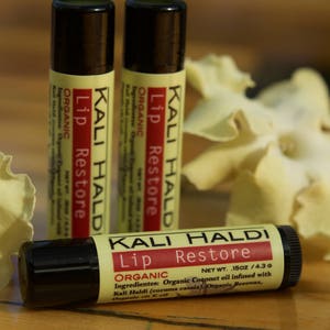 May include: Three tubes of Kali Haldi Lip Restore organic lip balm. The tubes are black with white and red text. The lip balm is 1.5 oz / 4.3 g. The lip balm is made with organic coconut oil infused with Kali Haldi (turmeric) and organic beeswax.