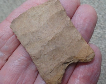May include: A tan-colored, chipped stone arrowhead with a triangular shape. The arrowhead has a rough, textured surface and appears to be made of a natural stone material. The edges are sharp and the overall form is well-defined.