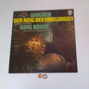 May include: A vintage vinyl record album cover featuring the text "WAGNER DER RING DES NIBELUNGEN" in yellow and green. The album cover has a dark background with a gold-colored, ornate design. The album is titled "KARL BOHM Orchestral Highlights".