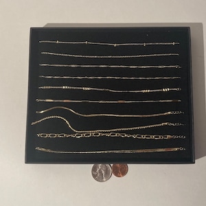 May include: A black box with a velvet interior displays a collection of gold chains of various styles and lengths. Two UK coins are visible in the foreground.