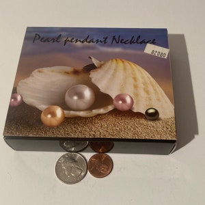 May include: A box containing a pearl pendant necklace. The box features an image of a seashell with pearls inside. The text on the box reads "Pearl pendant Necklace" and "62080".
