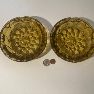 Pode incluir: Dois cinzeiros de vidro âmbar com um padrão geométrico em relevo. Os cinzeiros são redondos e têm uma ligeira borda.