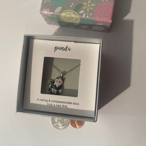 May include: A silver necklace with a black and white panda charm. The necklace is in a white box with a white card that says "panda" and "A caring & compassionate soul, truly a rare find."
