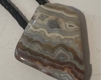 May include: A bolo tie with a brown, white, and gray agate stone pendant. The bolo tie cord is black leather.