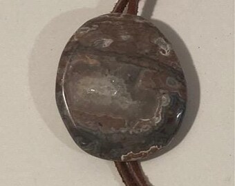Può includere: Una collana con cordoncino in pelle marrone con un ciondolo rotondo in agata marrone e bianco.