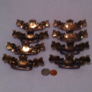 May include: Ten antique brass drawer pulls with ornate designs. The pulls are arranged in two rows of five.