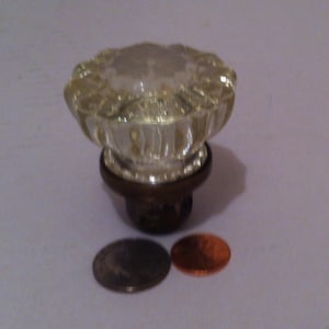 May include: A clear glass door knob with a brass base. The knob is faceted and has a starburst pattern. The knob is shown next to two UK coins for scale.