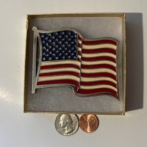 Peut inclure: Une boucle de ceinture argentée avec un motif de drapeau américain en émail. Le drapeau est rouge, blanc et bleu avec des étoiles sur le champ bleu. La boucle est dans une petite boîte.