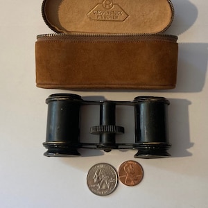 May include: Vintage black binoculars with a brown leather case. The case has a zipper closure and the text "REDENSTOCK MUNCHEN" on the inside.