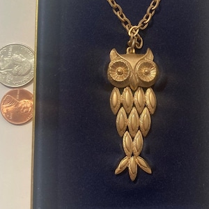 May include: A gold owl pendant necklace in a blue velvet box. The owl is detailed with scales and has large, round eyes.