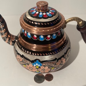 May include: A traditional Turkish copper teapot with a black base and intricate floral designs painted in blue, red, and yellow. The teapot has a wooden handle and a copper lid with a decorative finial.