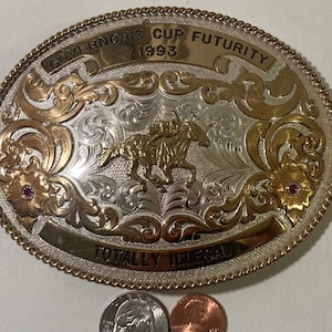 Pode incluir: Fivela de cinto de prata com detalhes em ouro e ouro rosa. A fivela apresenta um cavalo e um cavaleiro, e o texto "Governor's Cup Futurity 1993" e "Totally Illegal".