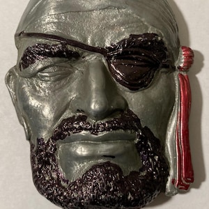 May include: A silver-colored pirate face mask with a black eyepatch and a red bandana. The mask has a detailed beard and mustache.