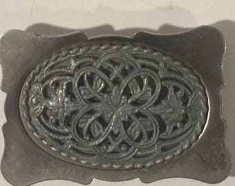 Könnte beinhalten: Eine silberfarbene Gürtelschnalle mit einem filigranen Blumendesign.