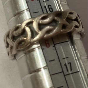 May include: Silver ring with a Celtic knot design, measured on a ruler showing size 6.5.