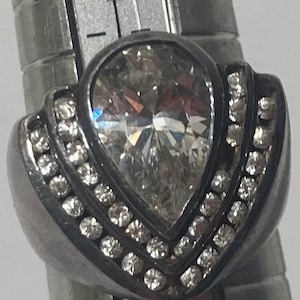 May include: A silver ring with a large pear-shaped clear stone surrounded by smaller clear stones.