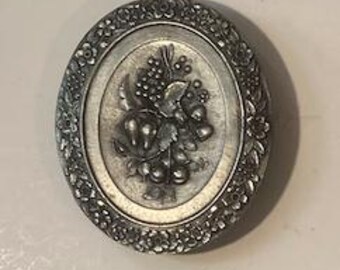 Könnte beinhalten: Eine ovale Silber-Schmuckdose mit einem erhabenen Design eines Blumenstraußes mit Beeren. Die Dose hat einen floralen Rand.