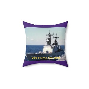 May include: Square pillow with a purple border featuring a photograph of the USS Stump (DD 978) naval destroyer at sea. The ship is gray with black antennas and is on a blue ocean under a blue sky.