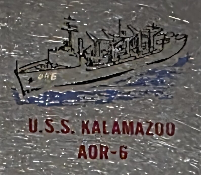 May include: A stylized illustration of the U.S.S. Kalamazoo AOR-6 naval vessel. The image features a detailed depiction of the ship, with the ship's name and designation in red text below the ship.