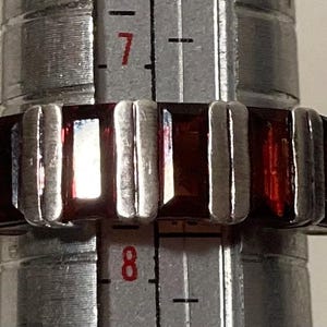 May include: A silver ring with multiple rectangular red gemstones. The ring is being measured with a ruler, showing the size is 7.