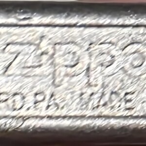 May include: Close-up of the bottom of a silver Zippo lighter. The text "Zippo" is prominently displayed, along with "BRADFORD, PA. MADE IN U.S.A." and the number "05". The lighter has a brushed metal finish.