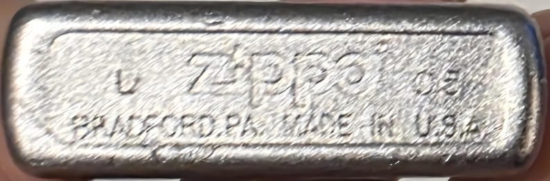 May include: Close-up of the bottom of a silver Zippo lighter. The text "Zippo" is prominently displayed, along with "BRADFORD, PA. MADE IN U.S.A." and the number "05". The lighter has a brushed metal finish.