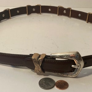 Puede incluir: Un cintur&oacute;n de cuero marr&oacute;n con una hebilla plateada y dorada. La hebilla tiene un dise&ntilde;o decorativo. El cintur&oacute;n mide 76 cm de largo.