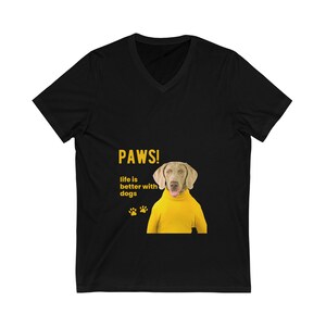 以下が含まれることがあります： 黄色のセーターを着た犬のグラフィックがプリントされた、黒いVネックTシャツ。Tシャツには「PAWS! Life is better with dogs」というテキストがプリントされています。