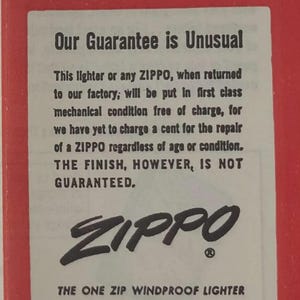 May include: A vintage advertisement for Zippo lighters. The text on the red and white paper reads "Our Guarantee is Unusual" and details the repair policy. The Zippo logo is prominently displayed, along with the company's address in Bradford, PA.