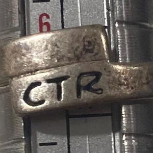 May include: A silver ring with the inscription "CTR" on the band.