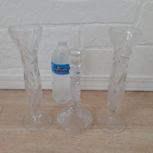 May include: Three clear glass vases with a diamond pattern. The vases are on a light wood surface. A clear plastic water bottle with the word "refreshe" printed on the label is in the center of the image.