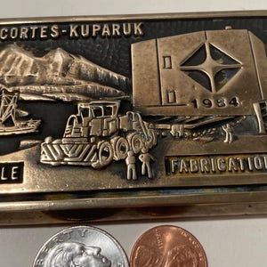 May include: A brass plaque with a relief image of a construction site. The plaque reads "Anacortes-Kuparuk Module Fabrication Site 1984".