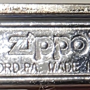 May include: Close-up of the bottom of a silver Zippo lighter. The text "Zippo" is prominently displayed, along with "BRADFORD PA. MADE IN U.S.A." and the number "05". The lighter has a shiny, reflective surface.