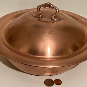 May include: A large copper serving dish with a domed lid and a brass handle. The dish is approximately 12 inches in diameter.