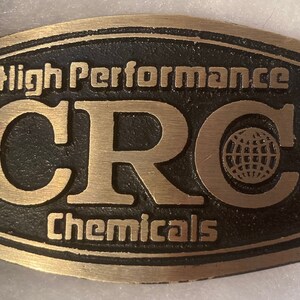 Peut inclure: Une boucle de ceinture en métal couleur or avec le texte "High Performance CRC Chemicals" et un graphique de globe.