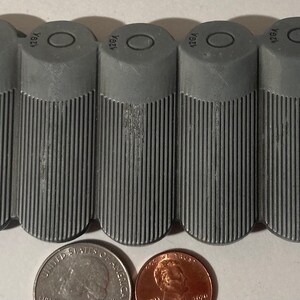 May include: Five gray cylindrical pill containers with a raised circle and the text "12GA" on the top of each container.