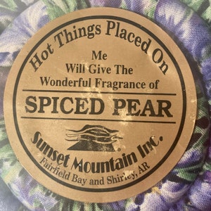 May include: A brown label with the text "Hot Things Placed On Me Will Give The Wonderful Fragrance of SPICED PEAR Sunset Mountain Inc. Fairfield Bay and Shirley, AR"