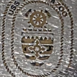 May include: A silver-toned emblem with the text "USS KALAMAZOO AOR-6" encircling a central design. The design includes a ship's wheel, a crest, and a cross-like symbol, all in a metallic gold color. The border has a rope-like texture.