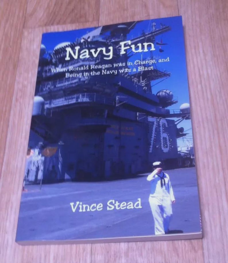 May include: A book titled "Navy Fun" with a navy ship and a sailor in uniform on the cover. The text reads "When Ronald Reagan was in Charge, and Being in the Navy was a Blast" and "Vince Stead". The cover is blue.