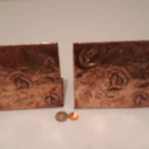 May include: A pair of copper bookends with an embossed design. The bookends are rectangular and have a textured surface.